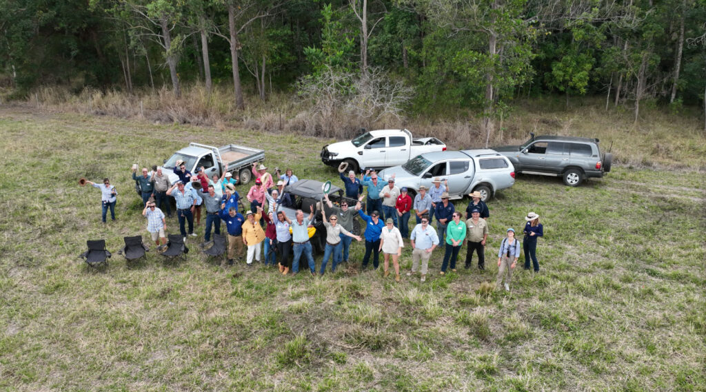 Group of people and some cars in a field waving up at drone camera