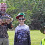 Man holding fish with a boy and another man at tilapia day in Mackay.