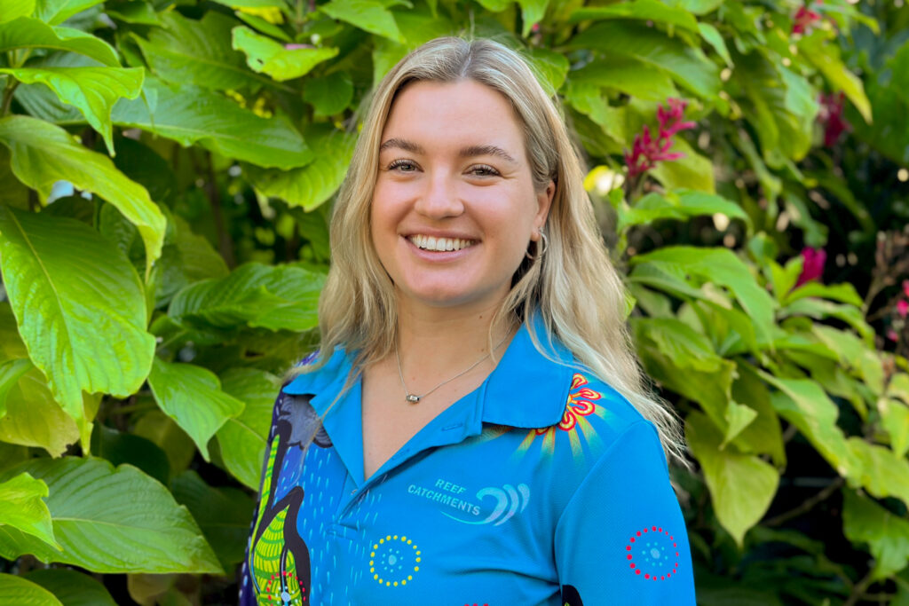 Alexandra Williams headshot - standing in front of a leafy green tree with purple flowers.