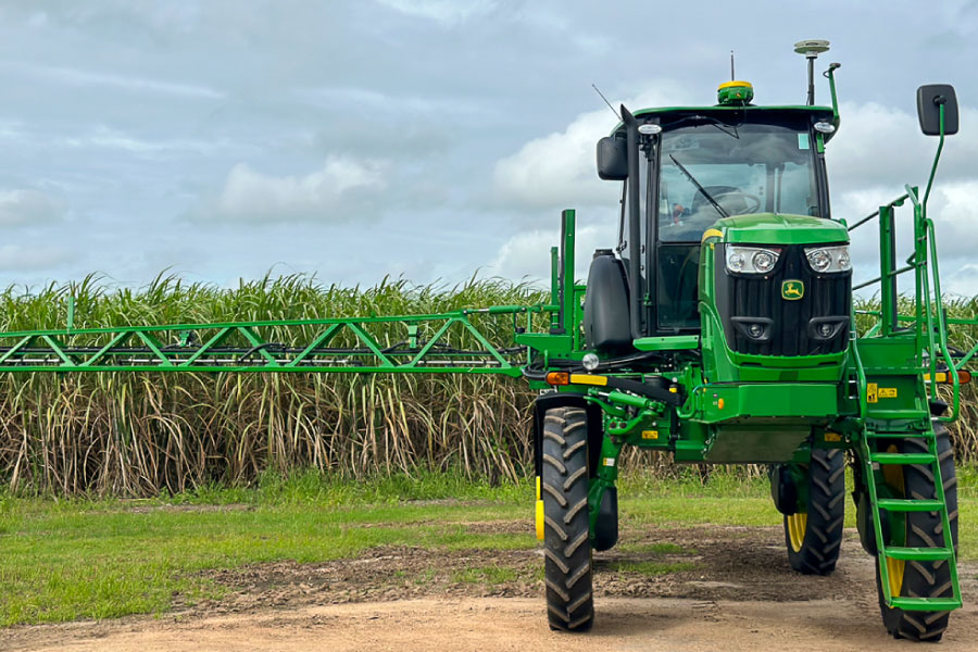 large green tractor with spray rig in front of sugar cane